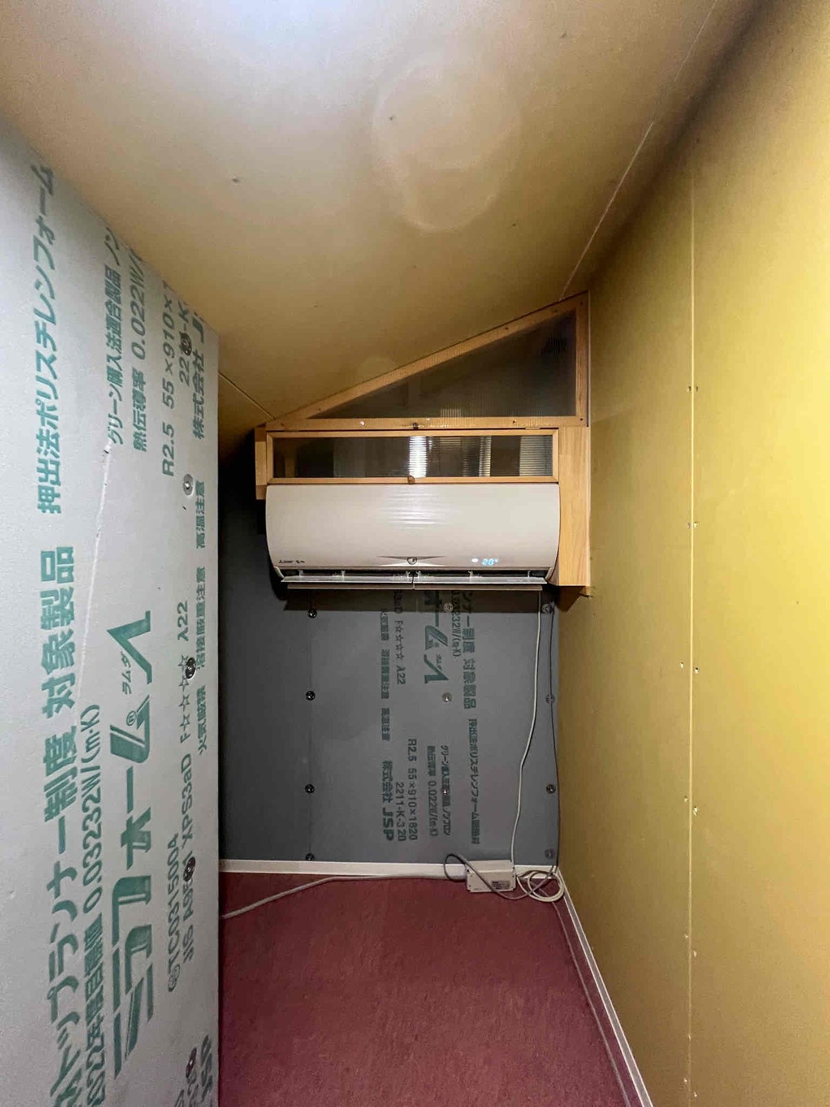 勾配天井の小屋裏に設置した壁掛けエアコン1台。断熱材の壁と床まで写る小屋裏空間の設置例